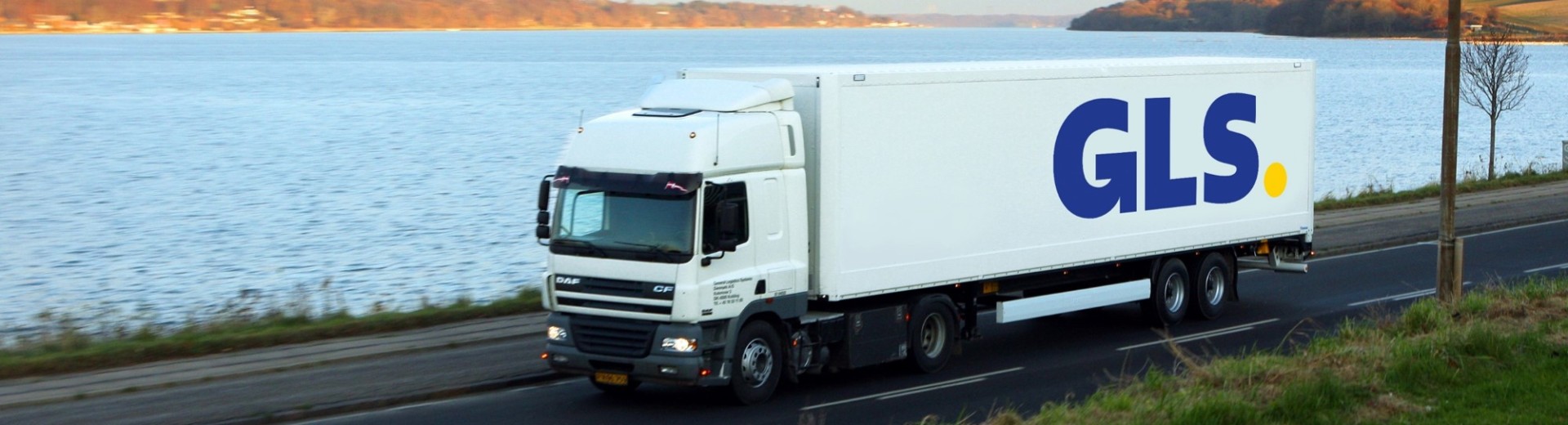A GLS truck driving along a road by the water